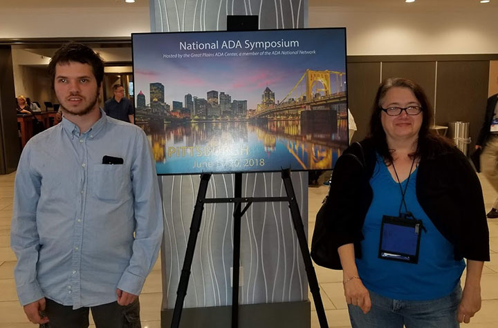 Mack Kelleher and Vivian Drobnak with a National ADA Symposium sign of the Pittsburgh skyline at night