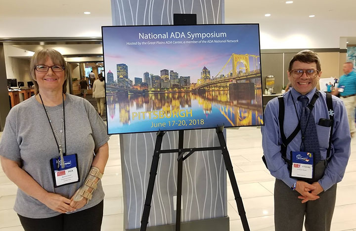 Marlene Kuser and R.V. Kuser with a National ADA Symposium sign of the Pittsburgh skyline at night