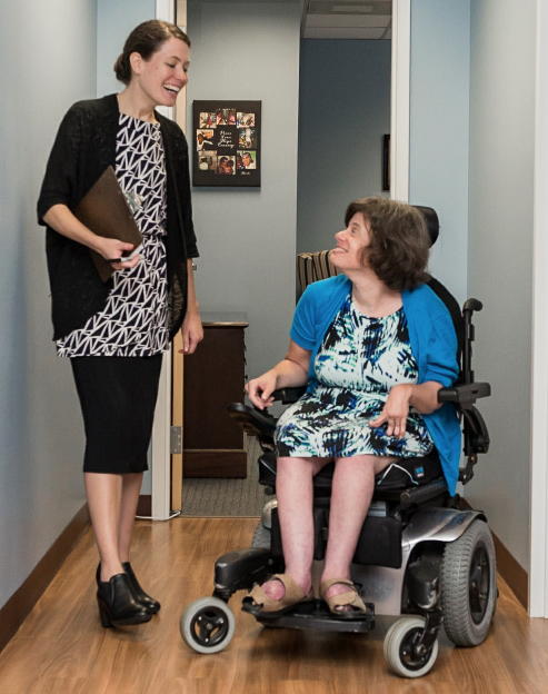 Woman walking side-by-side with woman with disabilities in a wheelchair discussing an issue.