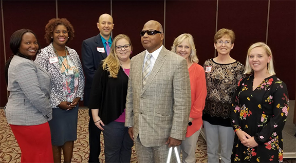 Group photo featuring Mayor’s Committee members and presenter Ashley Hayes Chassereau (in the middle wearing glasses, a black jacket, and a purple shirt), Community Employment Program Specialist at the NC Division of Vocational Rehabilitation Services